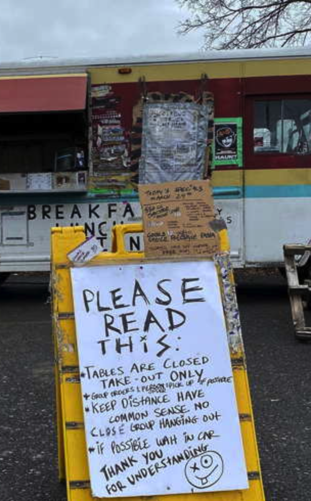 Yellow A-frame sign with take-out and closure notices in front of a food truck
